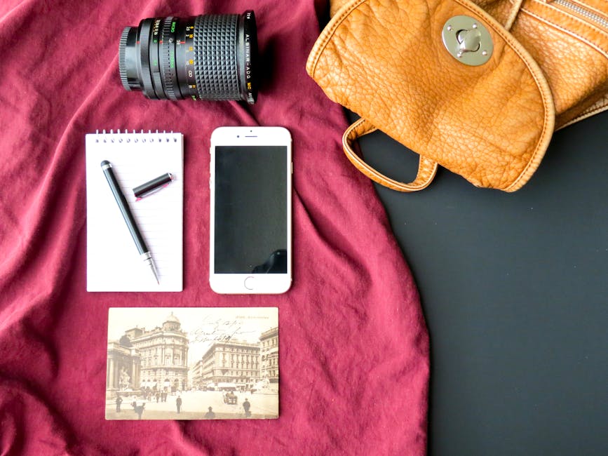 Flat lay of photography essentials with camera lens, smartphone, and leather bag on a red fabric backdrop.