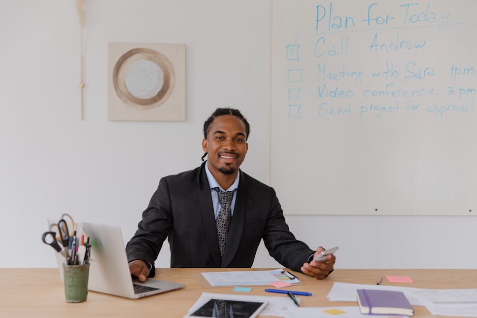 Professional man with braided hair working on a laptop in a modern office.