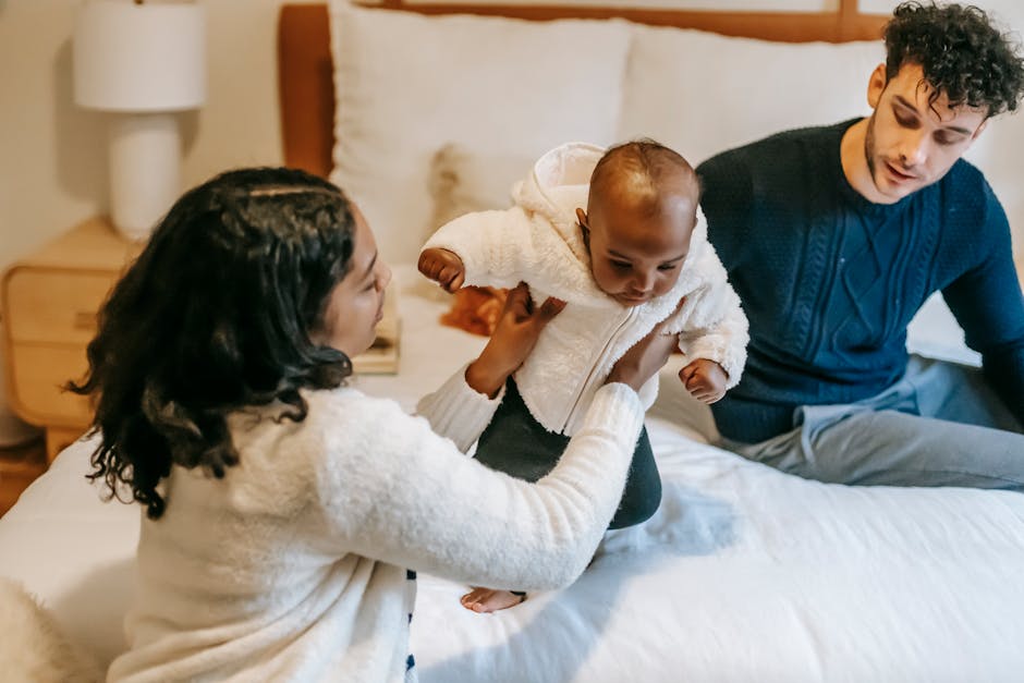 High angle of caring African American mom holding cute baby sitting on bed with father