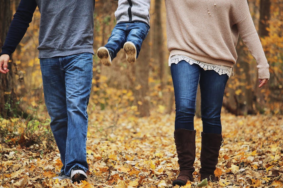 Family enjoying a playful autumn walk in a forest, lifting a child among colorful leaves.