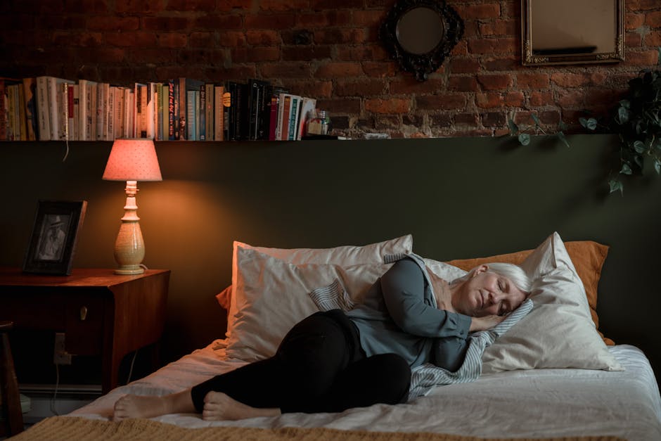 Elderly woman peacefully sleeping in a cozy bedroom with a lamp and books at night.