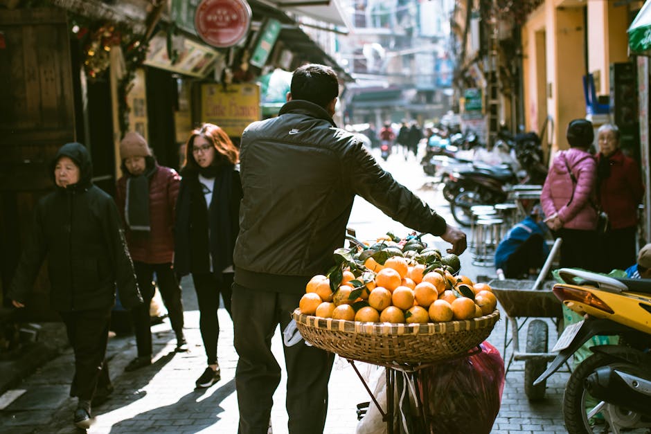 A busy street scene in Hanoi with a vendor selling fresh oranges.