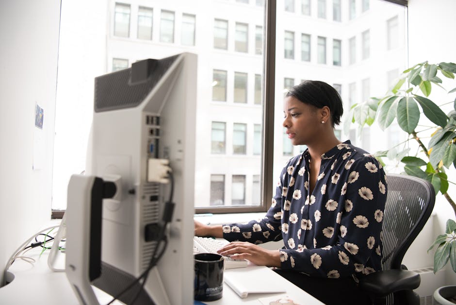 Professional woman typing in a modern office with large windows and indoor plants.