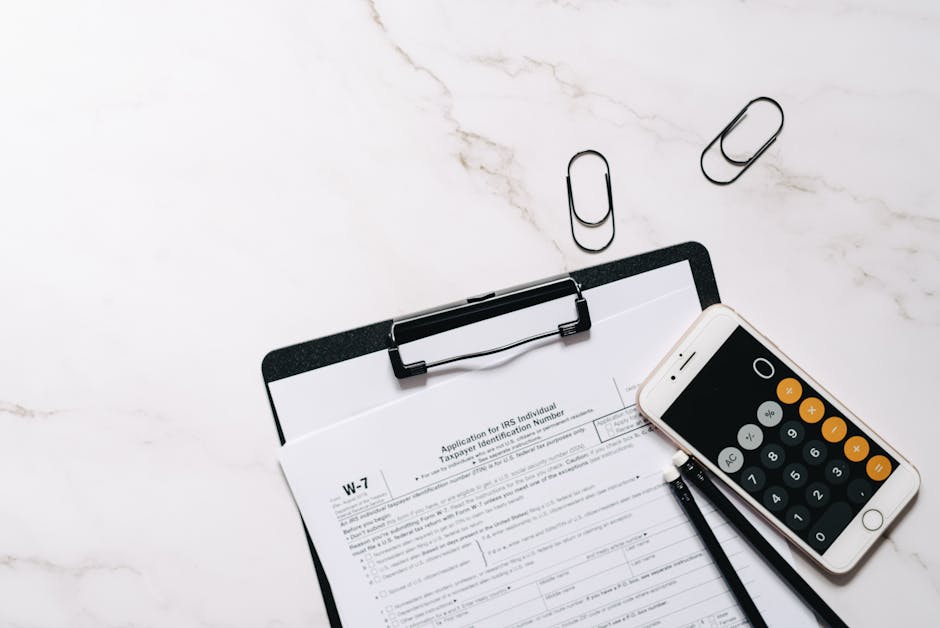 A flat lay of W-7 IRS form, smartphone calculator, and paper clips for tax preparation.