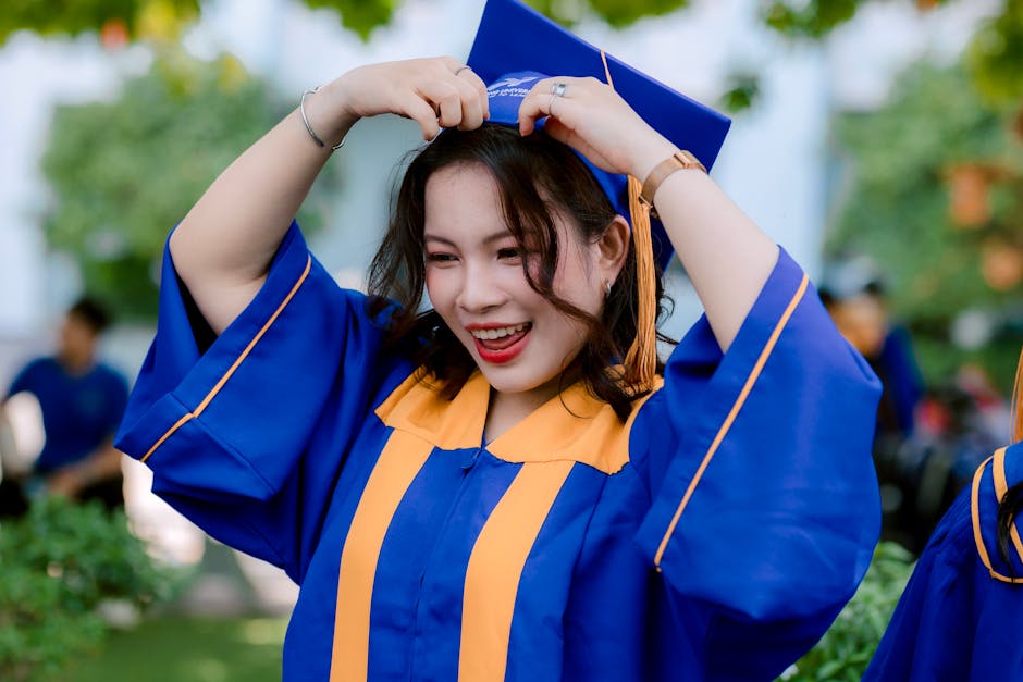 Young woman in blue and gold graduation gown celebrating outdoors.