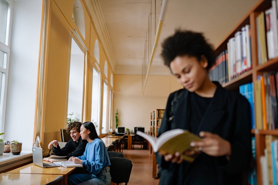 Students engaged in study sessions inside a university library, focusing on books and laptops.