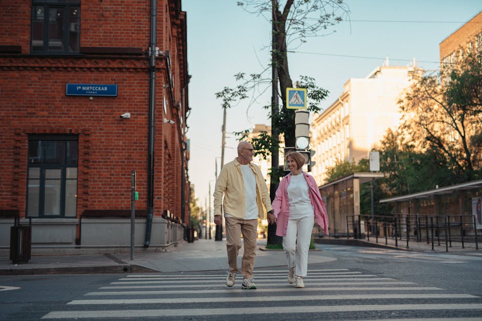 A joyful senior couple holding hands and strolling on a city crosswalk on a sunny day.