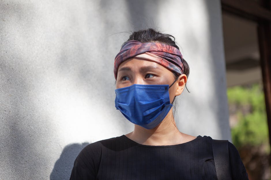 A close-up of an Asian woman wearing a blue face mask and black top, highlighting personal protective equipment.