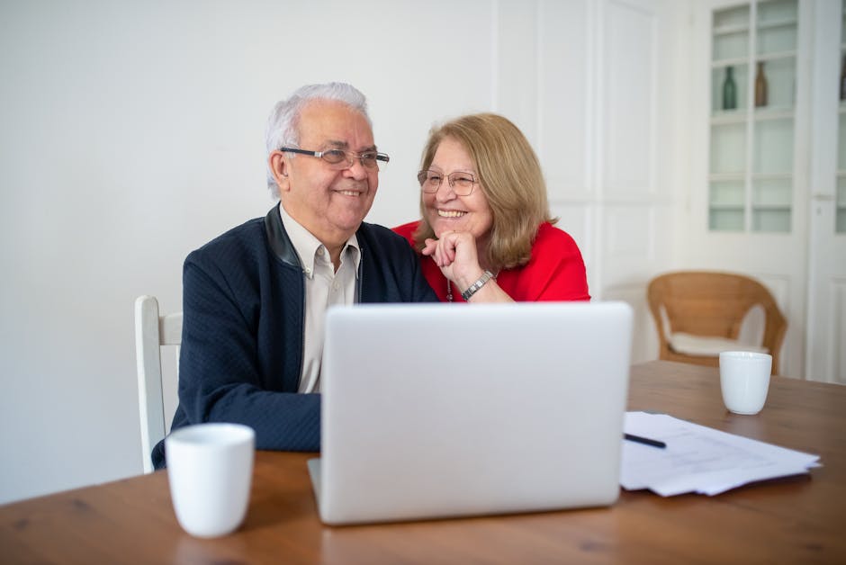 Senior couple smiling while using a laptop at home, enjoying online activities together.