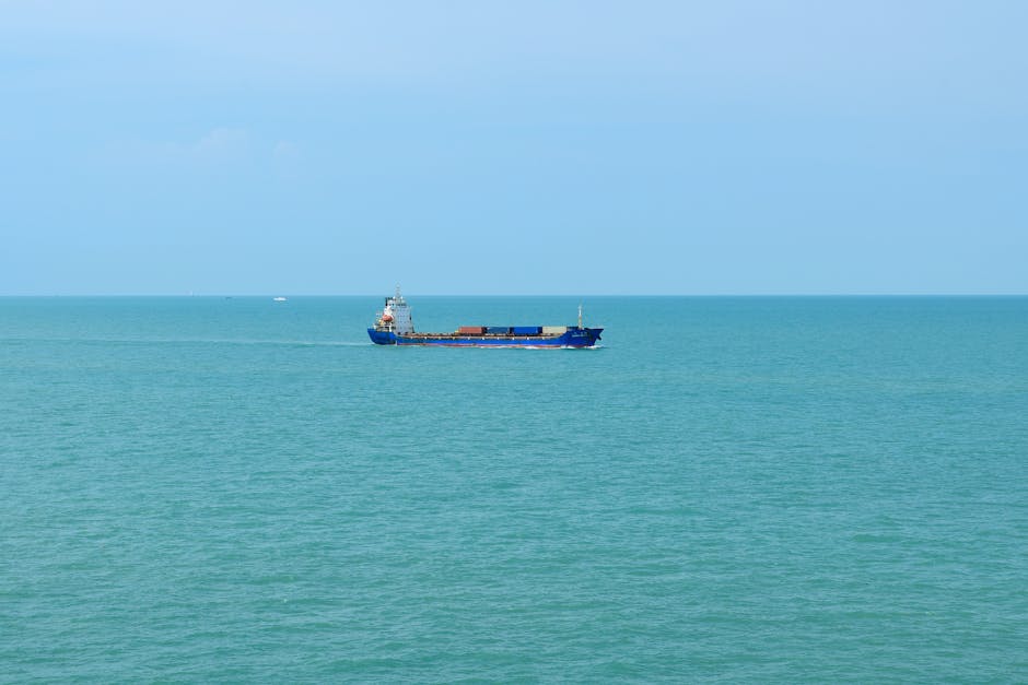 A solitary cargo ship sails in the tranquil blue ocean under a clear sky, conveying maritime trade.
