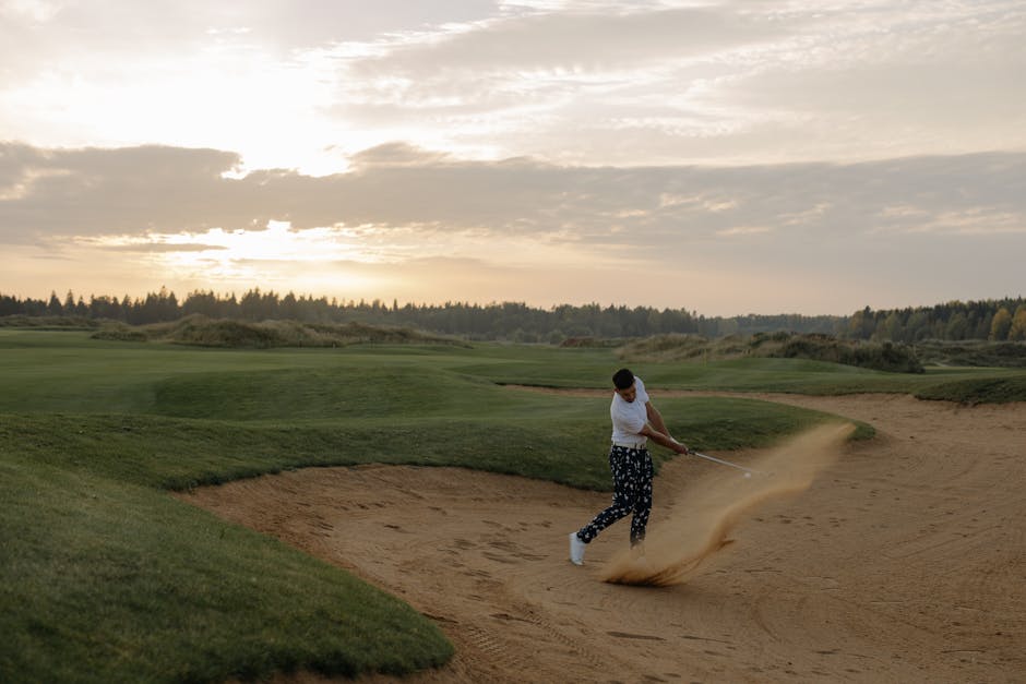 Golfer hitting a sand shot at sunset on a scenic golf course, showcasing skill and landscape.