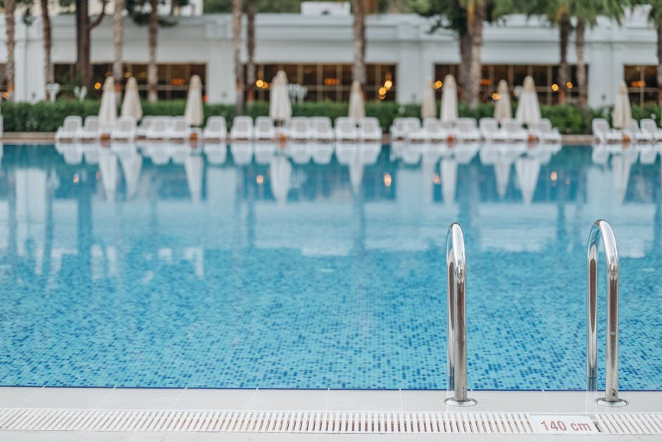 Bright and tranquil view of a resort swimming pool with ladder and deck chairs.
