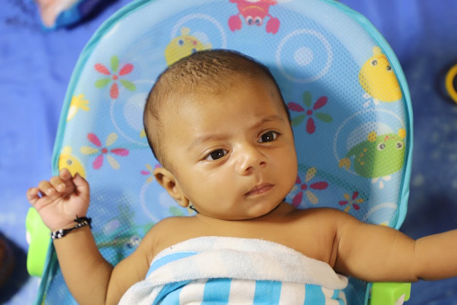 Cute baby wrapped in a striped towel resting in a colorful chair indoors.