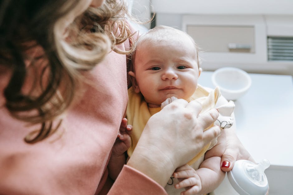 Crop unrecognizable mother embracing adorable little baby and bottle in light white room in daylight