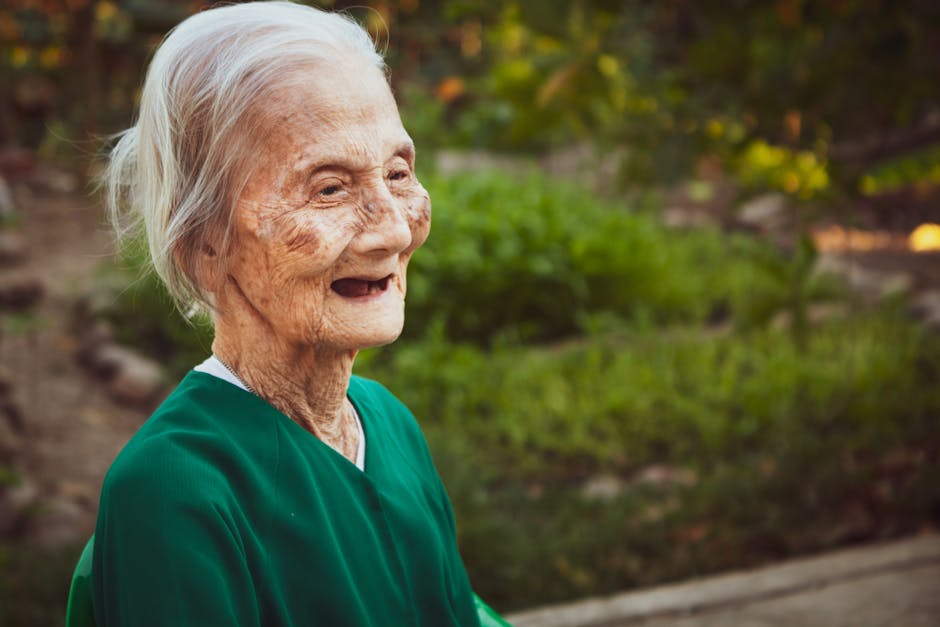 Positive elderly woman with wrinkles smiling with mouth opened while standing in green park
