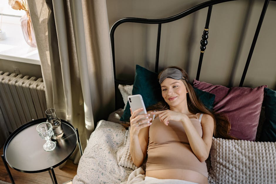Pregnant woman lying in bed with cellphone, enjoying a relaxing morning indoors.