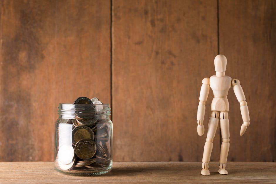 Wooden mannequin standing next to a jar filled with coins against a wooden backdrop, symbolizing savings and planning.