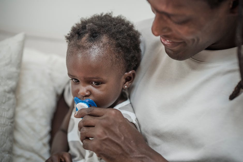 A father soothing his baby with a pacifier on a couch, capturing tender family moments.