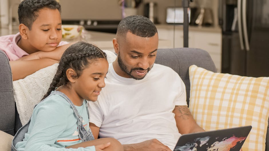 Father and two children bonding indoors on a couch, using a laptop. Happy family enjoying technology together.