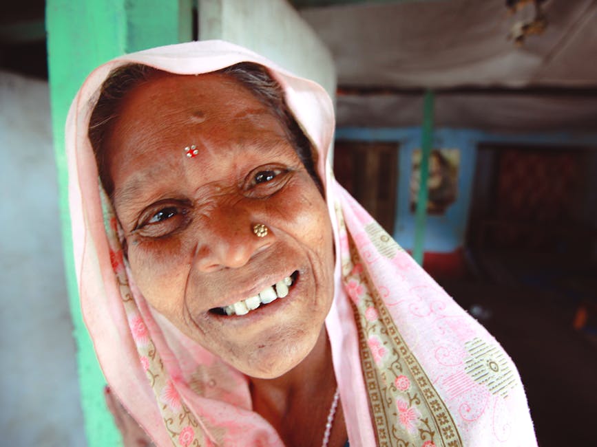 Elderly woman with a vibrant smile, wearing traditional attire and headscarf, indoors.