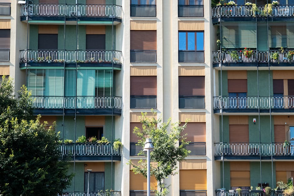 Contemporary apartment facade with glass balconies and green accents, capturing urban residential life.