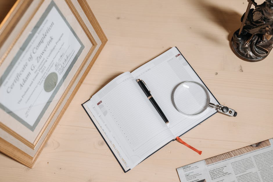 A tidy workspace featuring a certificate, open journal, magnifier, and statue on a wooden desk.