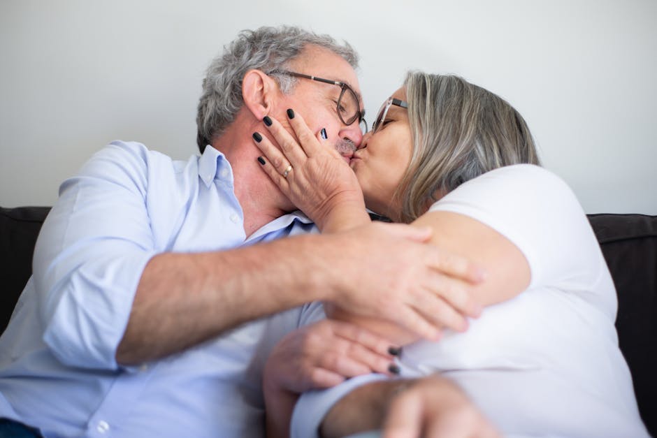 A senior couple in love shares a tender kiss on the couch, expressing affection and happiness.