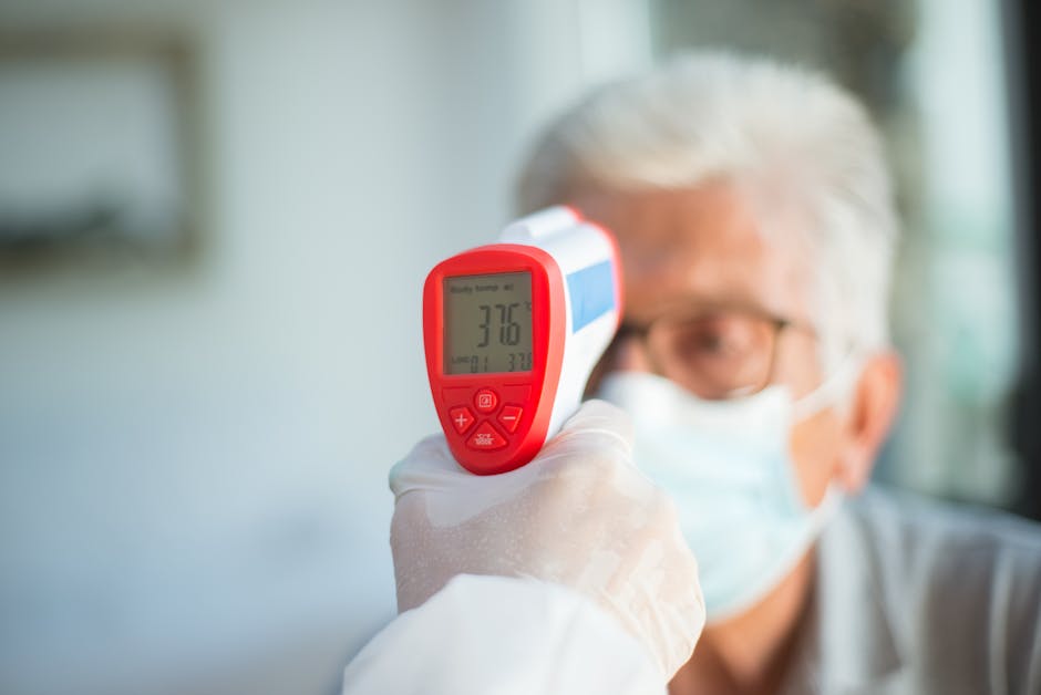 A healthcare professional uses a digital thermometer to check a senior patient's temperature indoors.