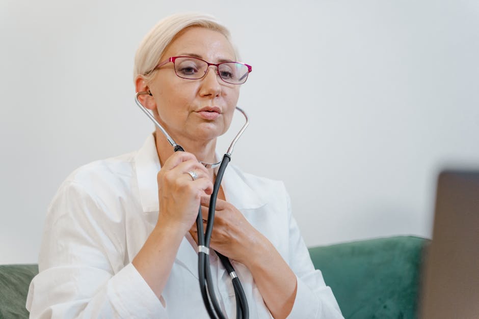Elderly female doctor using a stethoscope during a virtual consultation in a medical office.