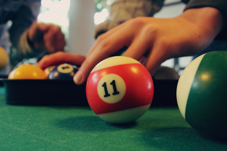 Close-up image of hands arranging billiard balls on a green pool table, focusing on a striped number 11 ball.