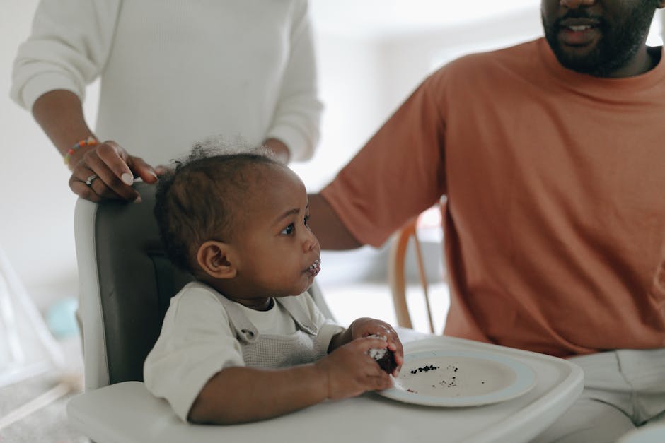 Black baby enjoying cake with family during first birthday celebration.