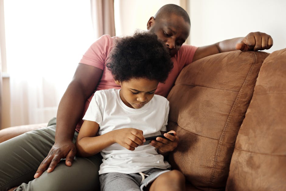 African American father and son bonding indoors while playing on smartphone. Capturing family leisure moments.