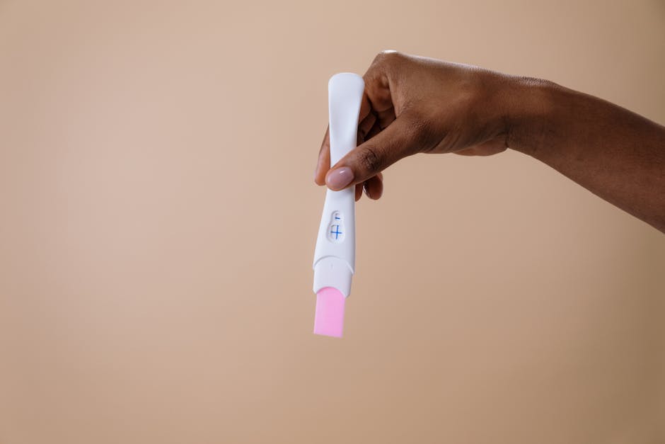 A woman's hand holding a positive pregnancy test on a neutral background.