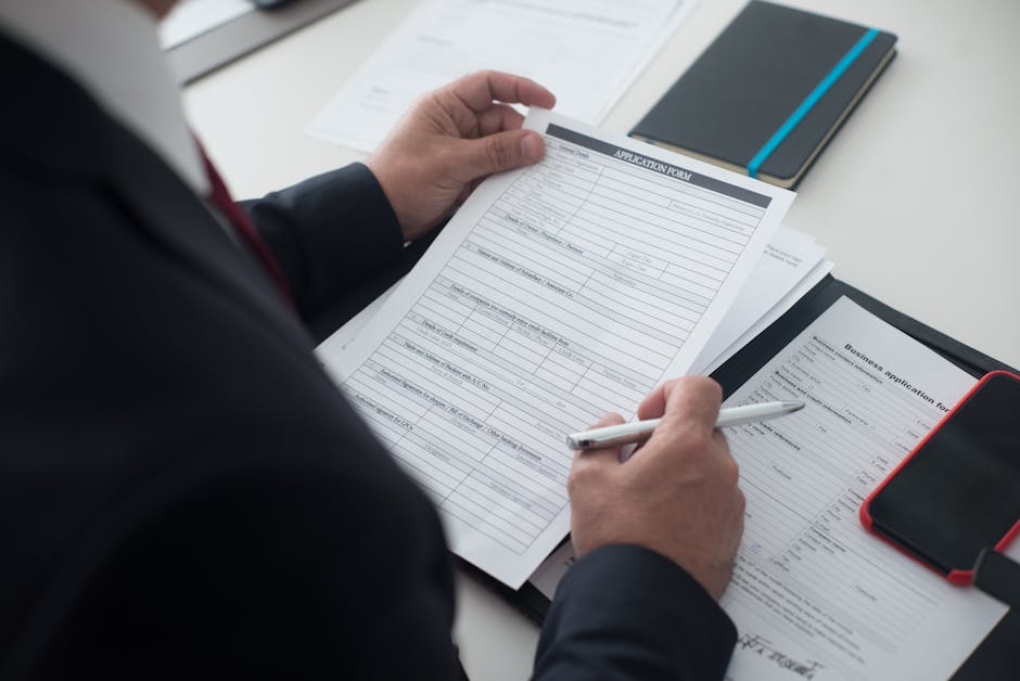 A businessman in a black suit reviews a printed application form with a pen on his desk.