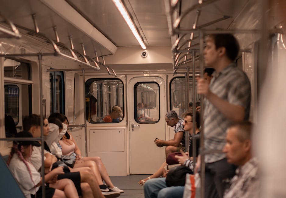 People sitting and standing in a subway train, engaging with phones and each other.