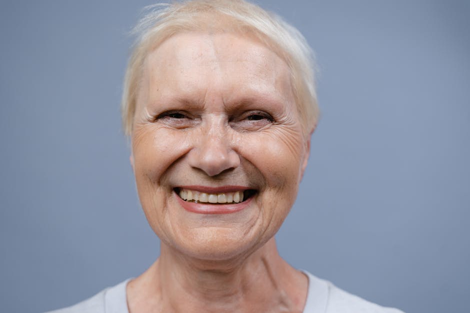 Close-up of a joyful elderly woman smiling with happiness against a blue background.