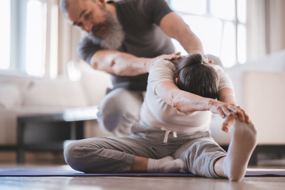 Senior couple practicing yoga at home with assistance, focusing on flexibility and wellness.