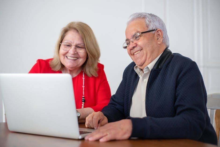 Elderly couple enjoying time together while using a laptop indoors, smiling and engaged.