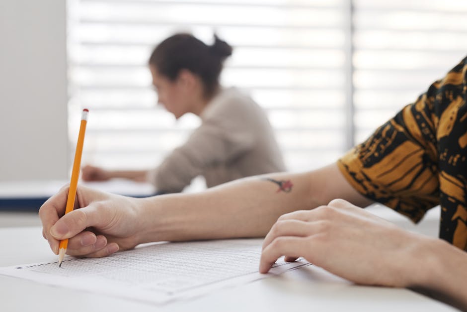 Close-up of student's hands writing on exam sheet, indoors with blurred background.