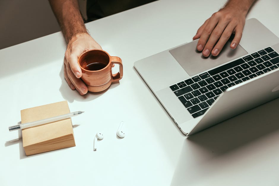 Minimalist workspace featuring a laptop, coffee mug, and AirPods for a modern work setup.