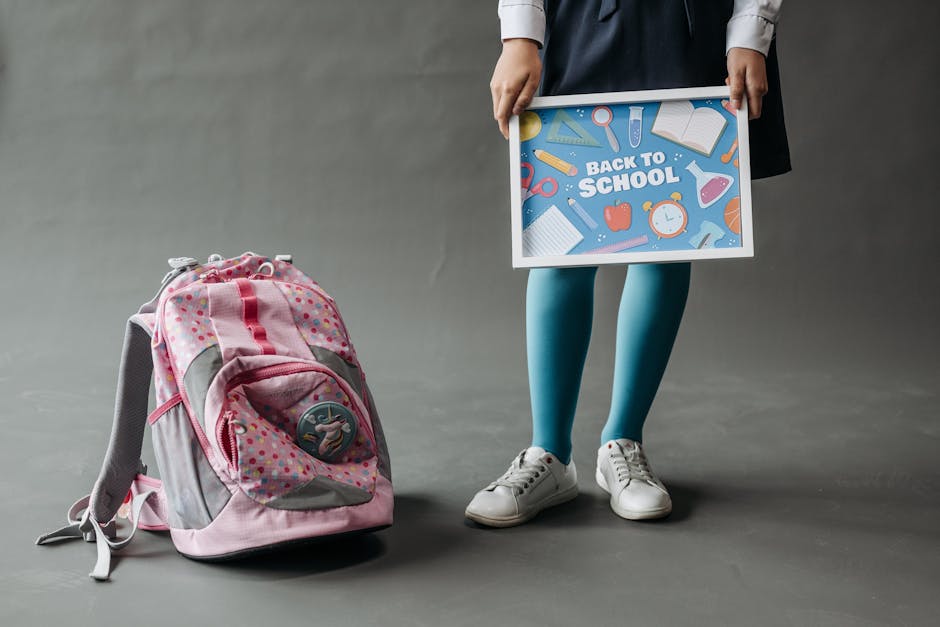 Child holding back to school sign, wearing uniform, with backpack. Studio photo.