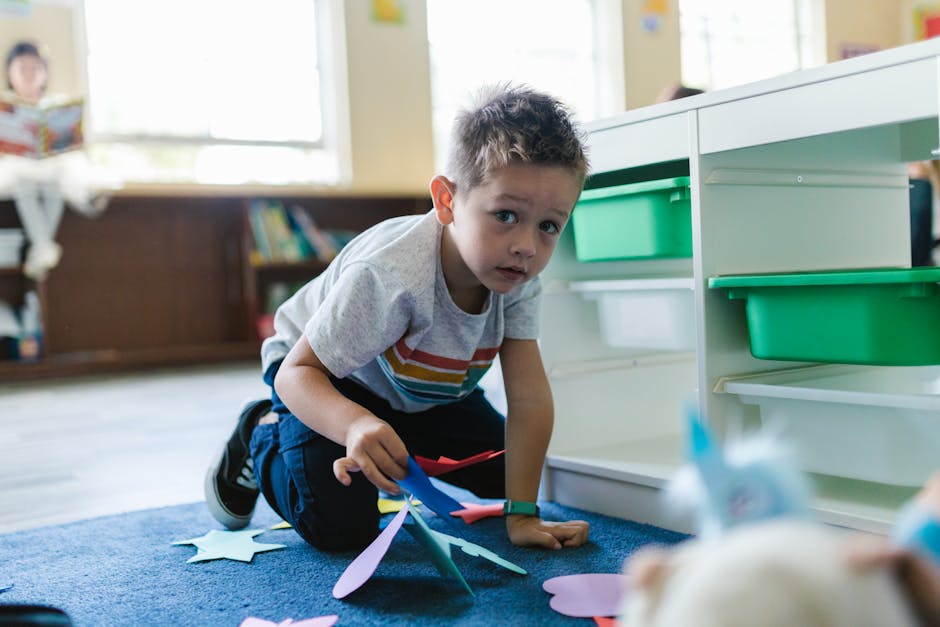 A young boy playing with colorful paper shapes on the classroom floor, showcasing early learning and creativity.