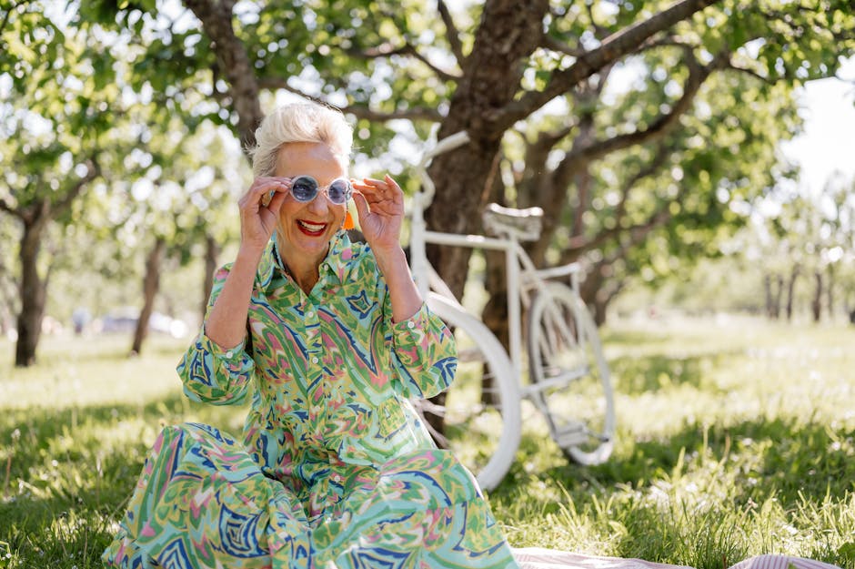 A joyful senior woman in a colorful dress smiles while outdoors, enjoying a sunny day with a bicycle.