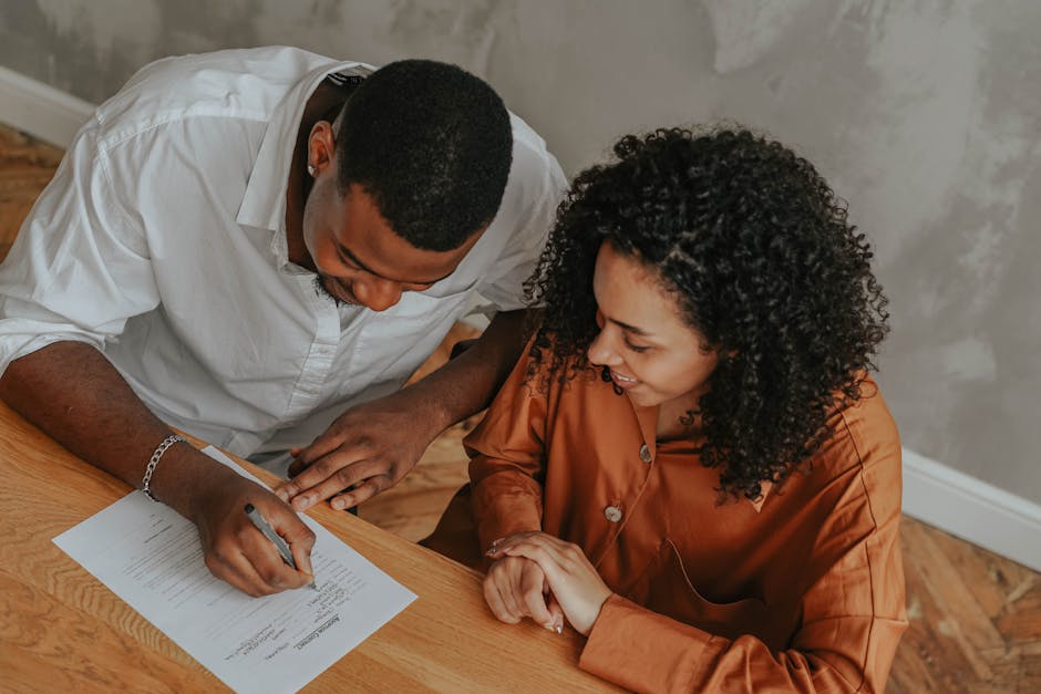 A couple signing an adoption certificate at a table, viewed from above.