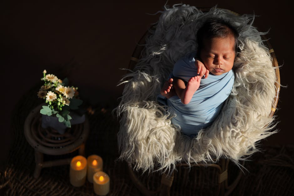 Snug newborn wrapped in blue, nestled on fuzzy blanket with candles and flowers beside.