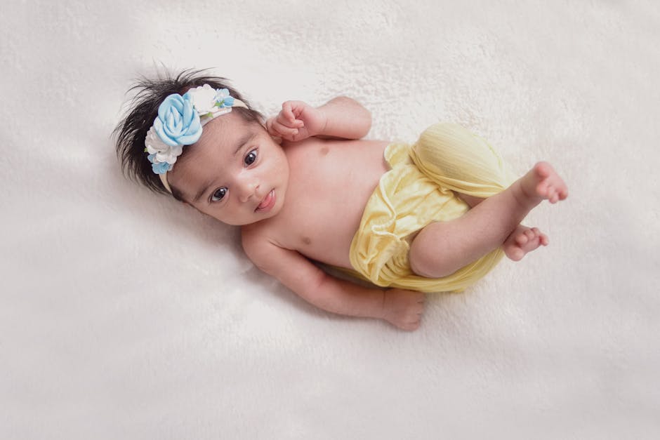 Cute baby lying on plush surface, wearing a blue floral headband and yellow swaddle.