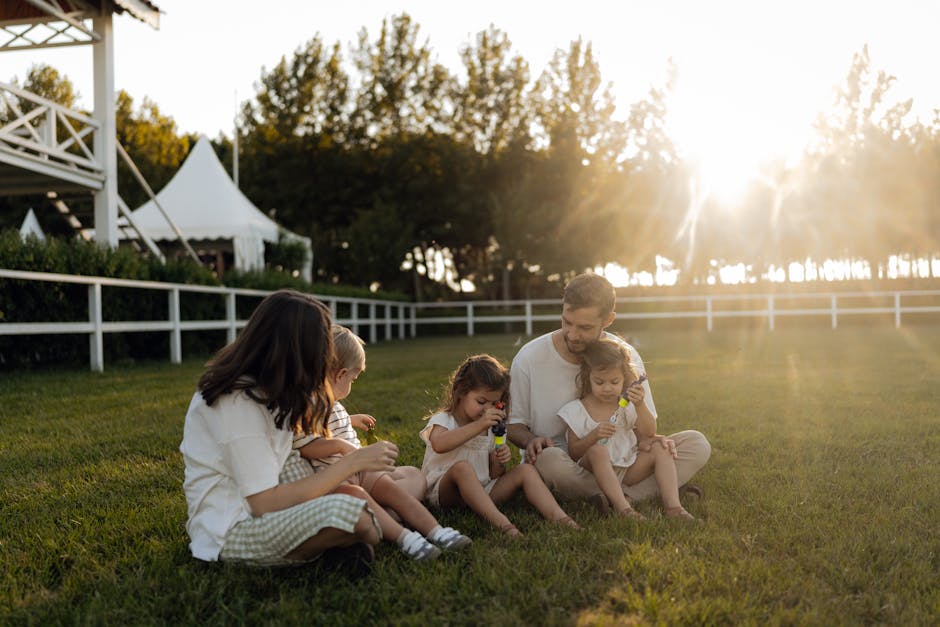 Family sitting on grass enjoying leisure time outdoors, with sun setting in the background.