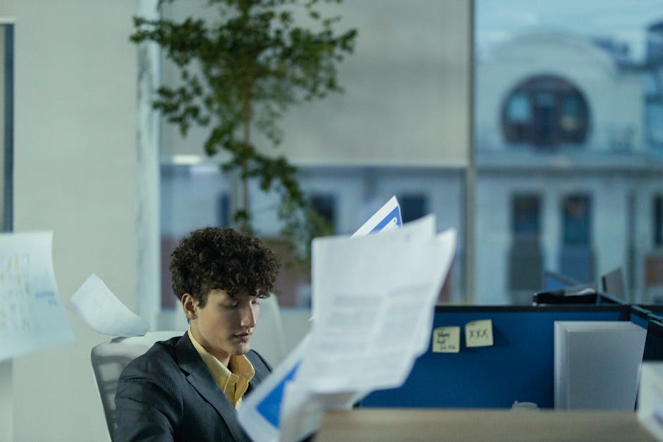 Young man in office cubicle tossing papers, illustrating busy work environment.