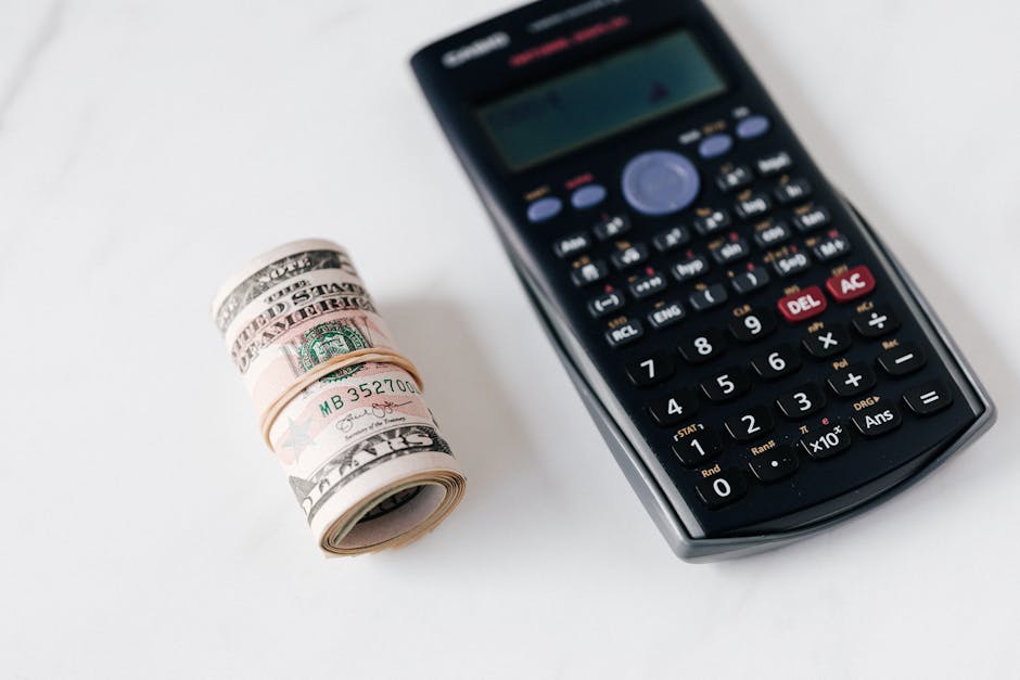 From above of modern electronic calculator with small display and buttons of different colors near roll of dollar bills on marble surface