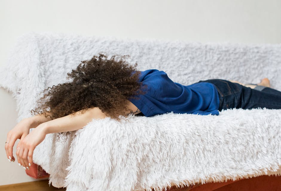 Woman with curly hair lying on a fluffy couch in a relaxed indoors setting.